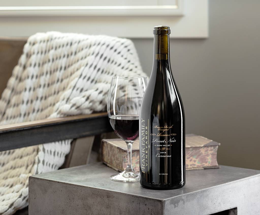 A glass of poured wine rests next to a bottle of Frank Family Pinot Noir