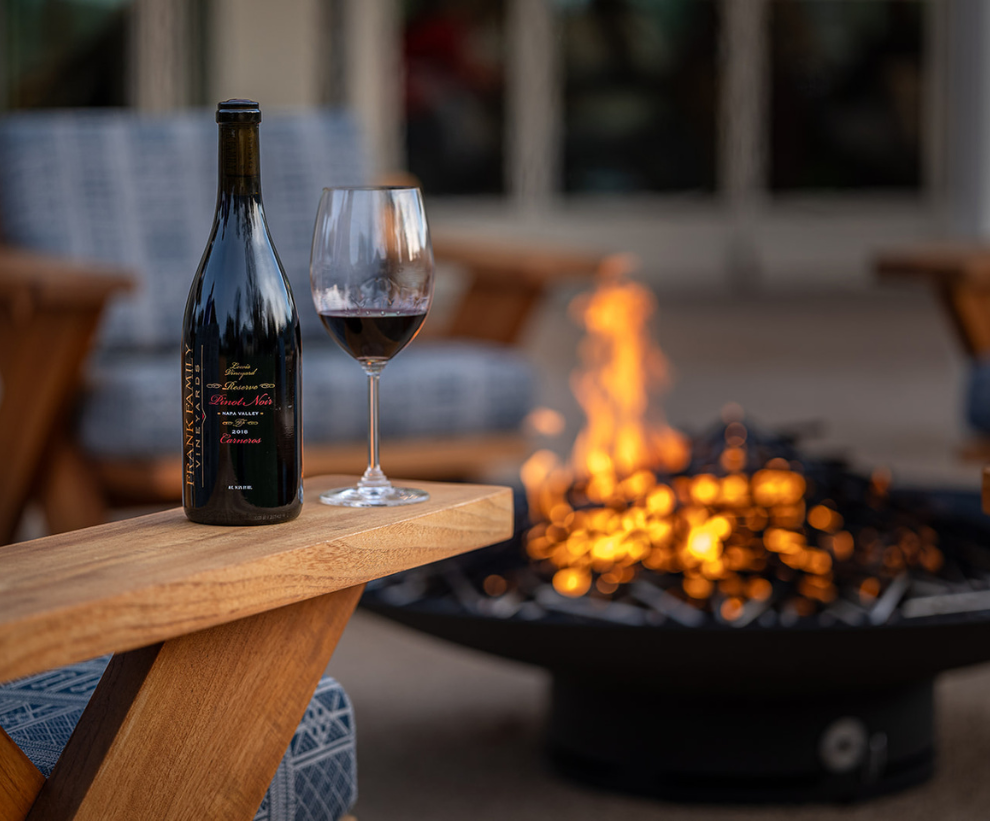 A bottle of Lewis Vineyard Pinot Noir next to a fire pit.