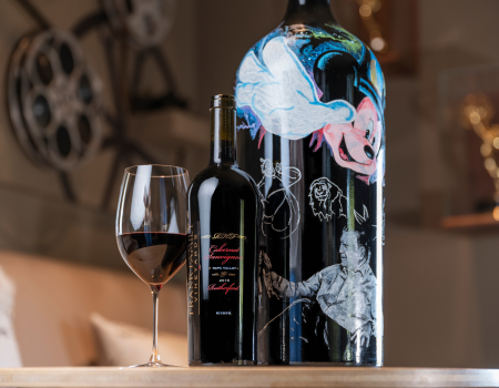 A bottle of Frank Family Vineyard's 2018 RHF Cabernet Sauvignon placed next to a custom portrait done of RIch Frank & Mickey Mouse, to commemorate his years at Disney.